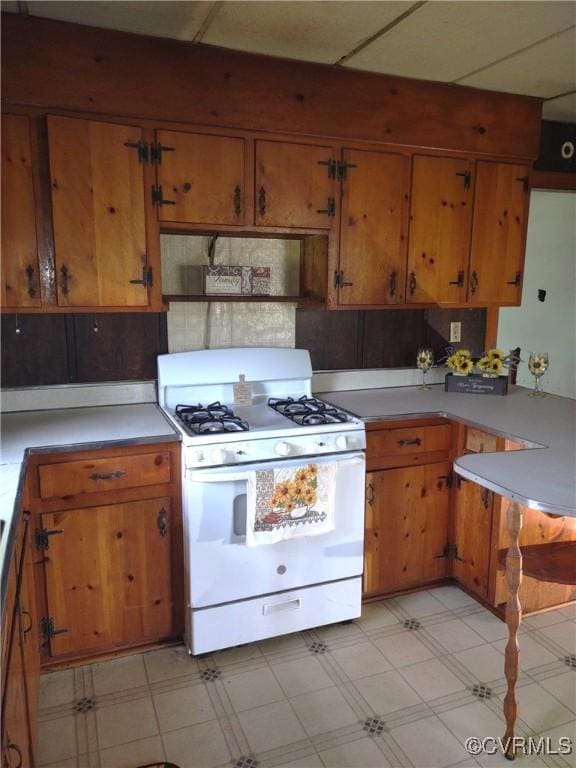 kitchen with white range with gas stovetop, brown cabinets, light countertops, light floors, and ventilation hood