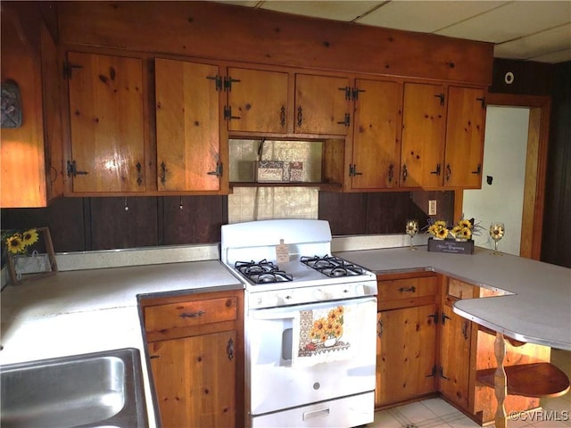 kitchen with white range with gas cooktop, brown cabinets, light countertops, and a peninsula