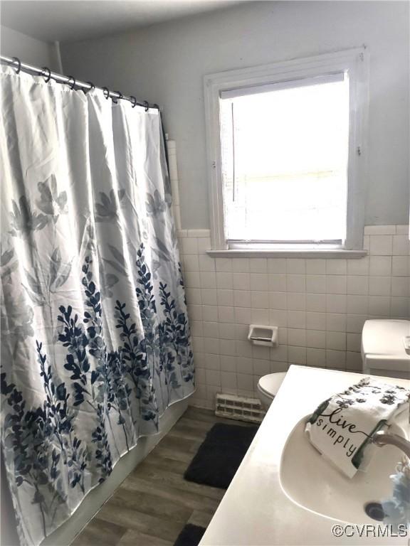 bathroom with tile walls, toilet, a wainscoted wall, curtained shower, and wood finished floors