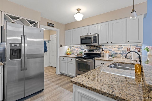 kitchen with appliances with stainless steel finishes, a sink, decorative backsplash, light wood-type flooring, and light stone countertops