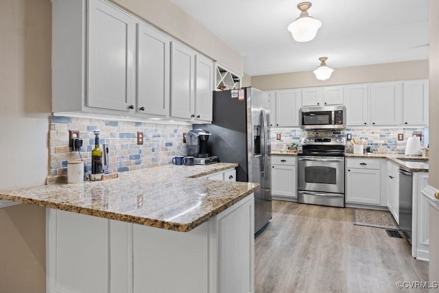 kitchen with stainless steel appliances, backsplash, a peninsula, and light stone countertops