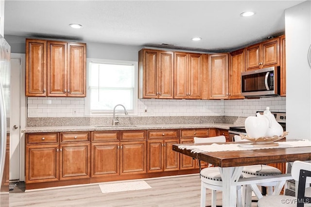 kitchen with appliances with stainless steel finishes, a sink, brown cabinets, and recessed lighting