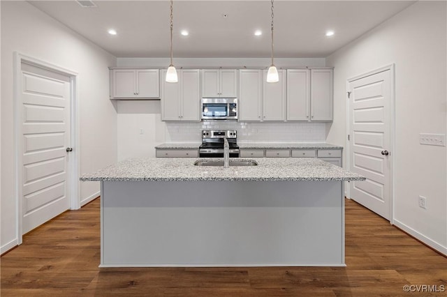 kitchen with appliances with stainless steel finishes, a sink, decorative backsplash, a center island with sink, and recessed lighting