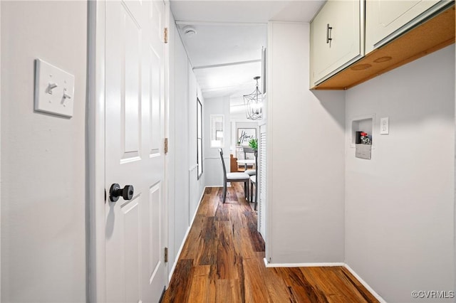 hallway with dark wood-style floors, baseboards, and a chandelier