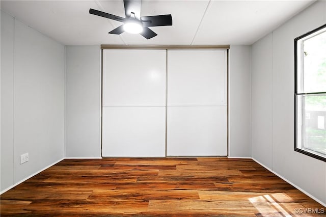 unfurnished bedroom featuring wood finished floors, multiple windows, ceiling fan, and a closet