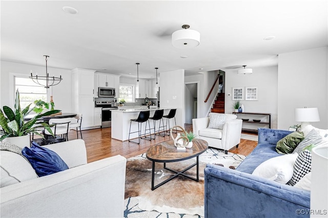 living room featuring stairs, a chandelier, and light wood finished floors