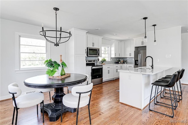 kitchen with stainless steel appliances, a chandelier, a sink, light wood finished floors, and light countertops