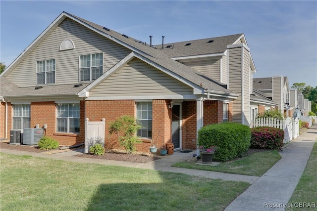 view of front of house with brick siding, cooling unit, and roof with shingles