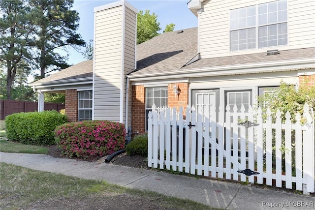 entrance to property featuring brick siding, fence, a shingled roof, and a chimney