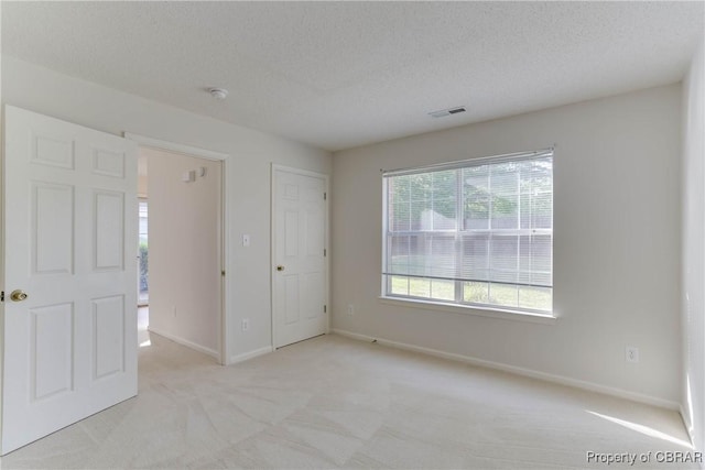 unfurnished bedroom featuring light colored carpet, baseboards, and a textured ceiling