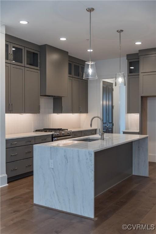 kitchen featuring gray cabinetry, a sink, an island with sink, light stone countertops, and backsplash