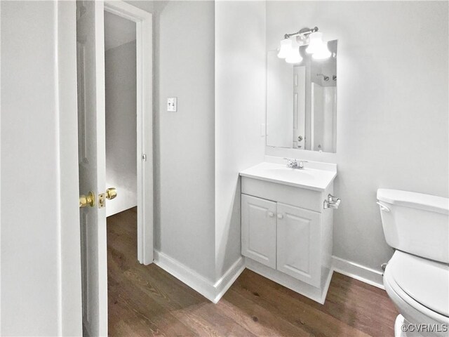 half bathroom featuring wood finished floors, toilet, baseboards, and vanity