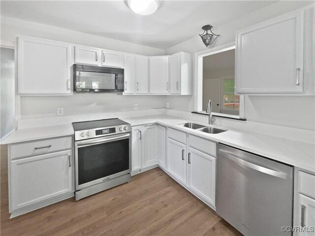 kitchen with stainless steel appliances, a sink, white cabinets, wood finished floors, and light countertops
