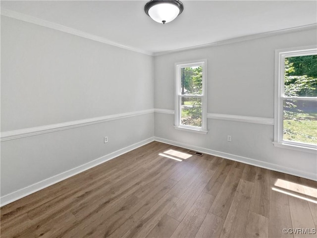 empty room featuring wood finished floors, baseboards, and ornamental molding