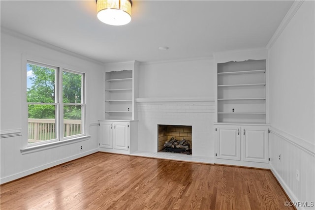 unfurnished living room with wood finished floors, built in shelves, a fireplace, and crown molding