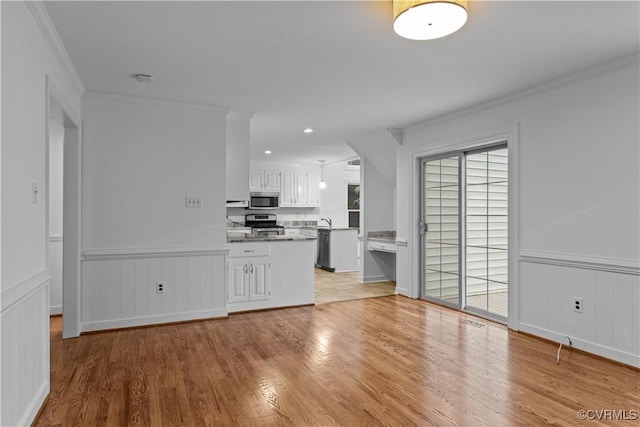 unfurnished living room with light wood-style flooring, wainscoting, crown molding, and a sink