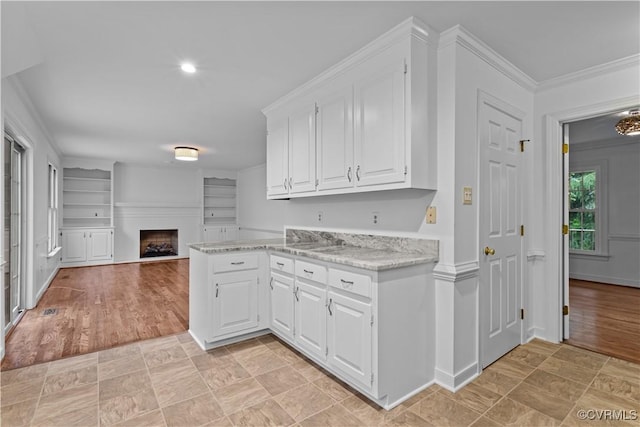 kitchen featuring white cabinetry, light stone countertops, open floor plan, crown molding, and a fireplace