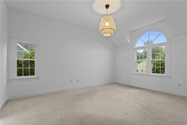 spare room featuring vaulted ceiling, light carpet, and baseboards