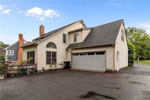 view of front of property featuring driveway, an attached garage, fence, a chimney, and a shingled roof