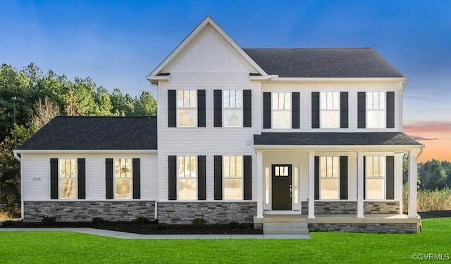 view of front of home with stone siding, a front lawn, a porch, and a shingled roof