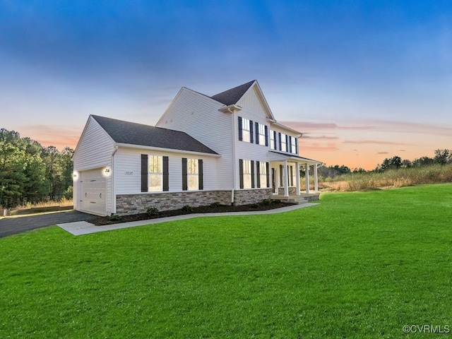 property exterior at dusk featuring a yard, stone siding, covered porch, asphalt driveway, and a garage