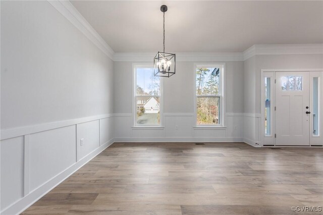unfurnished dining area with a chandelier, a wainscoted wall, ornamental molding, wood finished floors, and a decorative wall