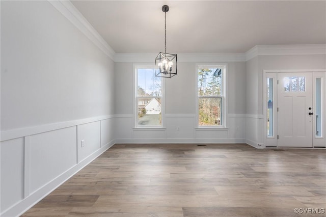 unfurnished dining area featuring a chandelier, wainscoting, ornamental molding, wood finished floors, and a decorative wall