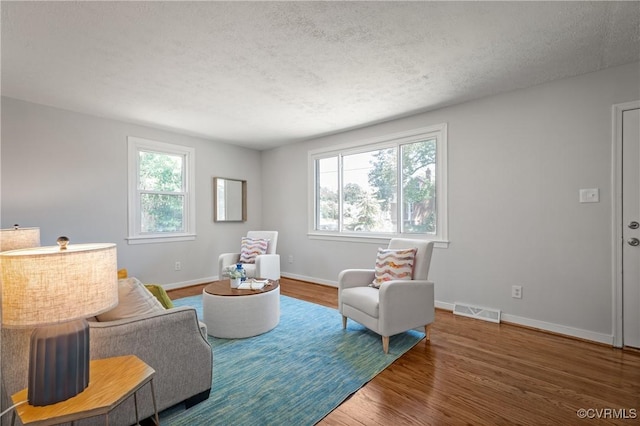living area with wood finished floors, a textured ceiling, and baseboards