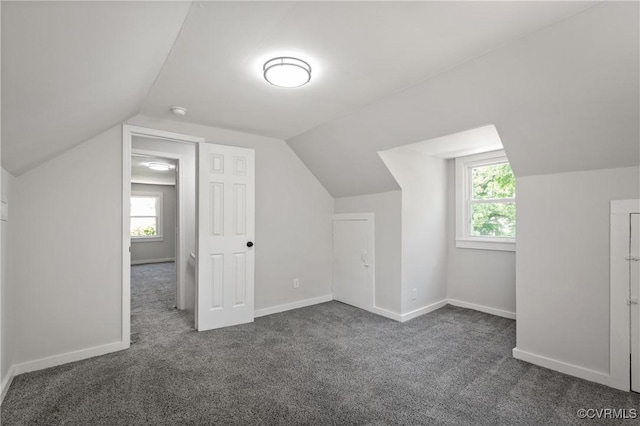additional living space featuring dark colored carpet, lofted ceiling, baseboards, and plenty of natural light