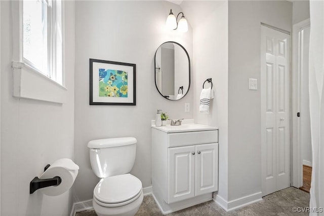 bathroom with baseboards, toilet, vanity, and a closet