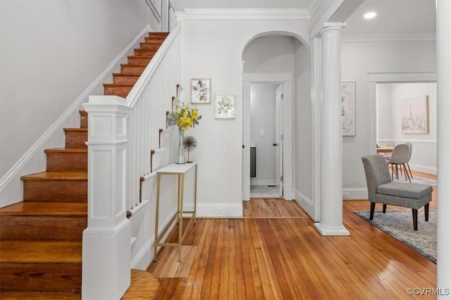 entrance foyer featuring ornate columns, light wood-style floors, baseboards, arched walkways, and stairs