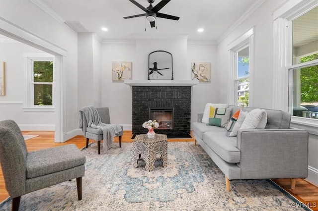 living area featuring healthy amount of natural light, wood finished floors, ceiling fan, a fireplace, and crown molding