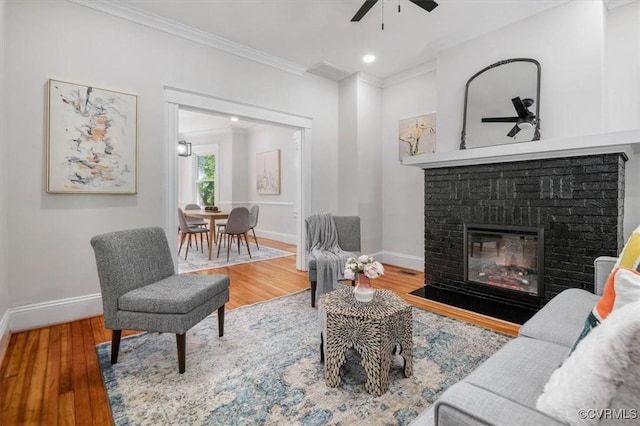 living room with ceiling fan, ornamental molding, wood finished floors, baseboards, and a fireplace