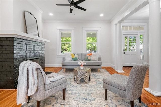 living area with ceiling fan, decorative columns, baseboards, wood finished floors, and a brick fireplace