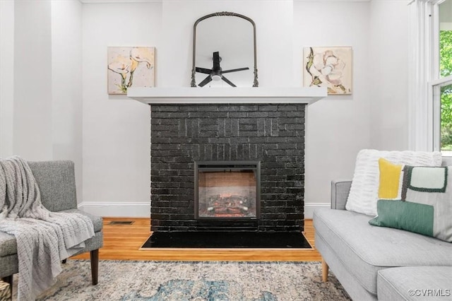 sitting room with a brick fireplace, baseboards, and wood finished floors