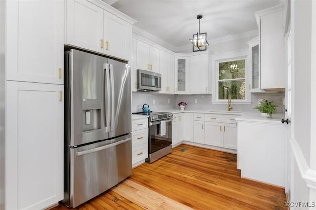 kitchen featuring stainless steel appliances, white cabinets, glass insert cabinets, light countertops, and crown molding