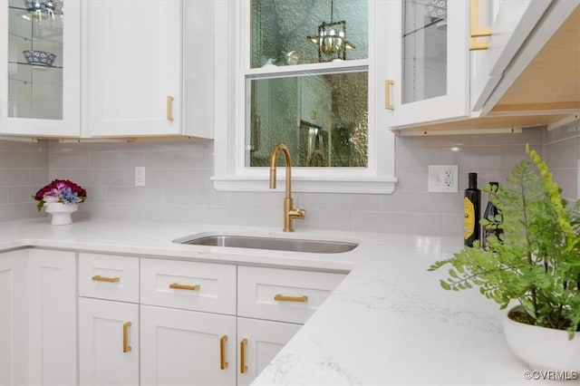 kitchen featuring a sink, white cabinetry, decorative backsplash, and glass insert cabinets