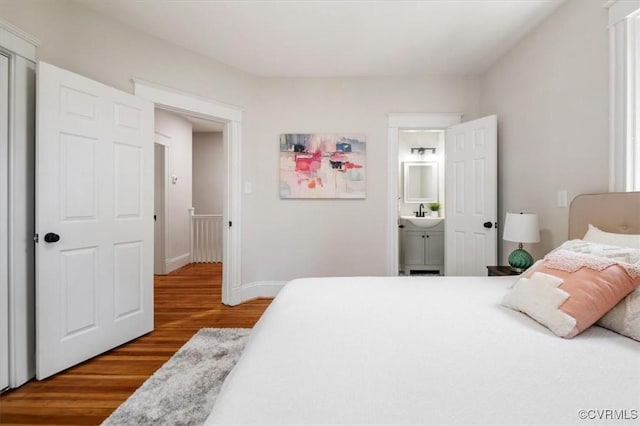 bedroom with wood finished floors, ensuite bathroom, baseboards, and a sink