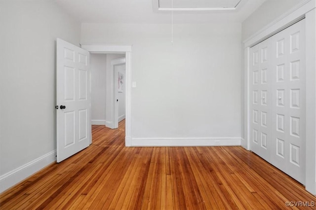 unfurnished bedroom with baseboards, a closet, light wood-style floors, and attic access