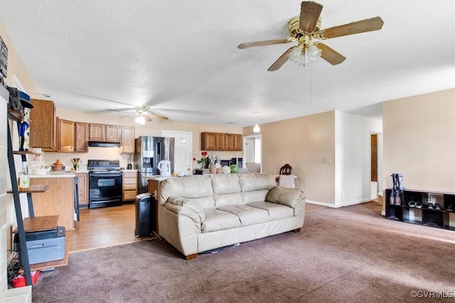 living room with ceiling fan, light colored carpet, a textured ceiling, and baseboards