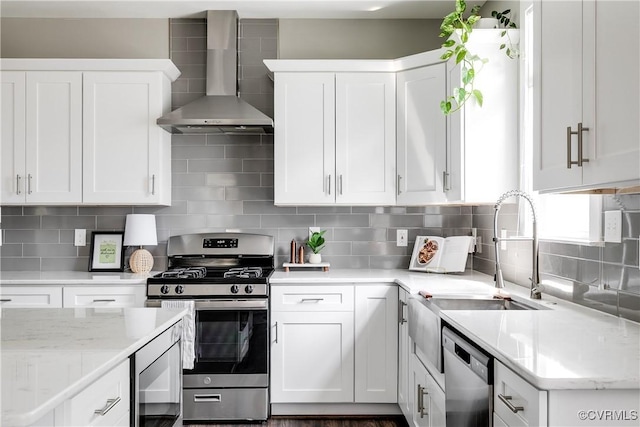kitchen featuring wall chimney range hood, stainless steel appliances, white cabinetry, a sink, and decorative backsplash