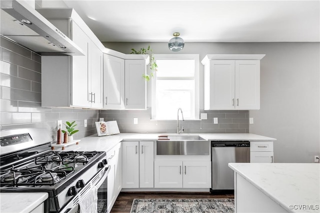 kitchen featuring stainless steel appliances, a sink, wall chimney exhaust hood, dark wood-type flooring, and white cabinets