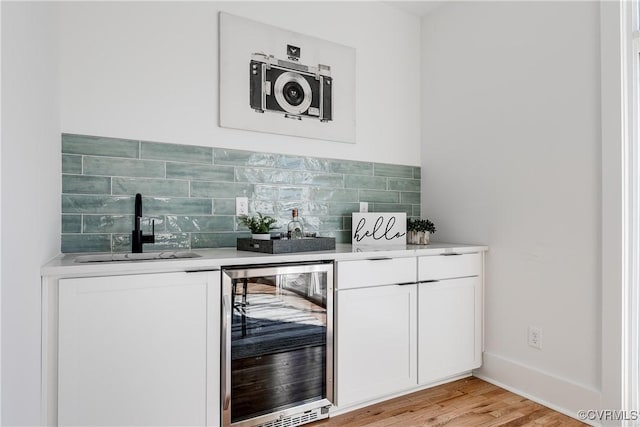 indoor wet bar with wine cooler, tasteful backsplash, and light wood finished floors