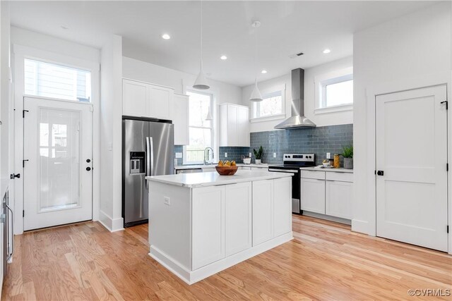 kitchen with appliances with stainless steel finishes, wall chimney exhaust hood, tasteful backsplash, light countertops, and white cabinets