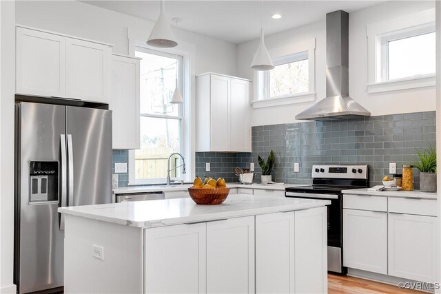 kitchen with stainless steel appliances, wall chimney range hood, white cabinets, a center island, and backsplash