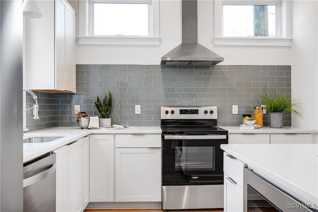 kitchen with stainless steel appliances, wall chimney range hood, a sink, wine cooler, and white cabinetry