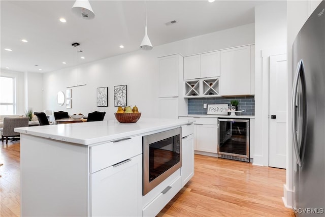 kitchen featuring beverage cooler, freestanding refrigerator, built in microwave, light wood finished floors, and white cabinetry