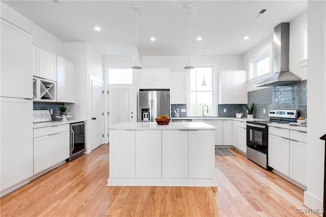 kitchen with stainless steel appliances, wall chimney exhaust hood, beverage cooler, a kitchen island, and light countertops
