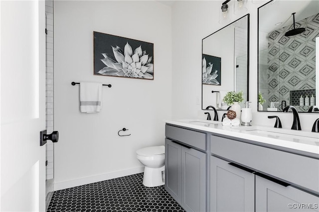 bathroom featuring toilet, a tile shower, double vanity, and baseboards