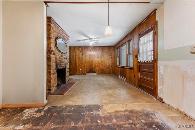 unfurnished living room featuring wooden walls, a fireplace, a ceiling fan, a baseboard heating unit, and baseboards